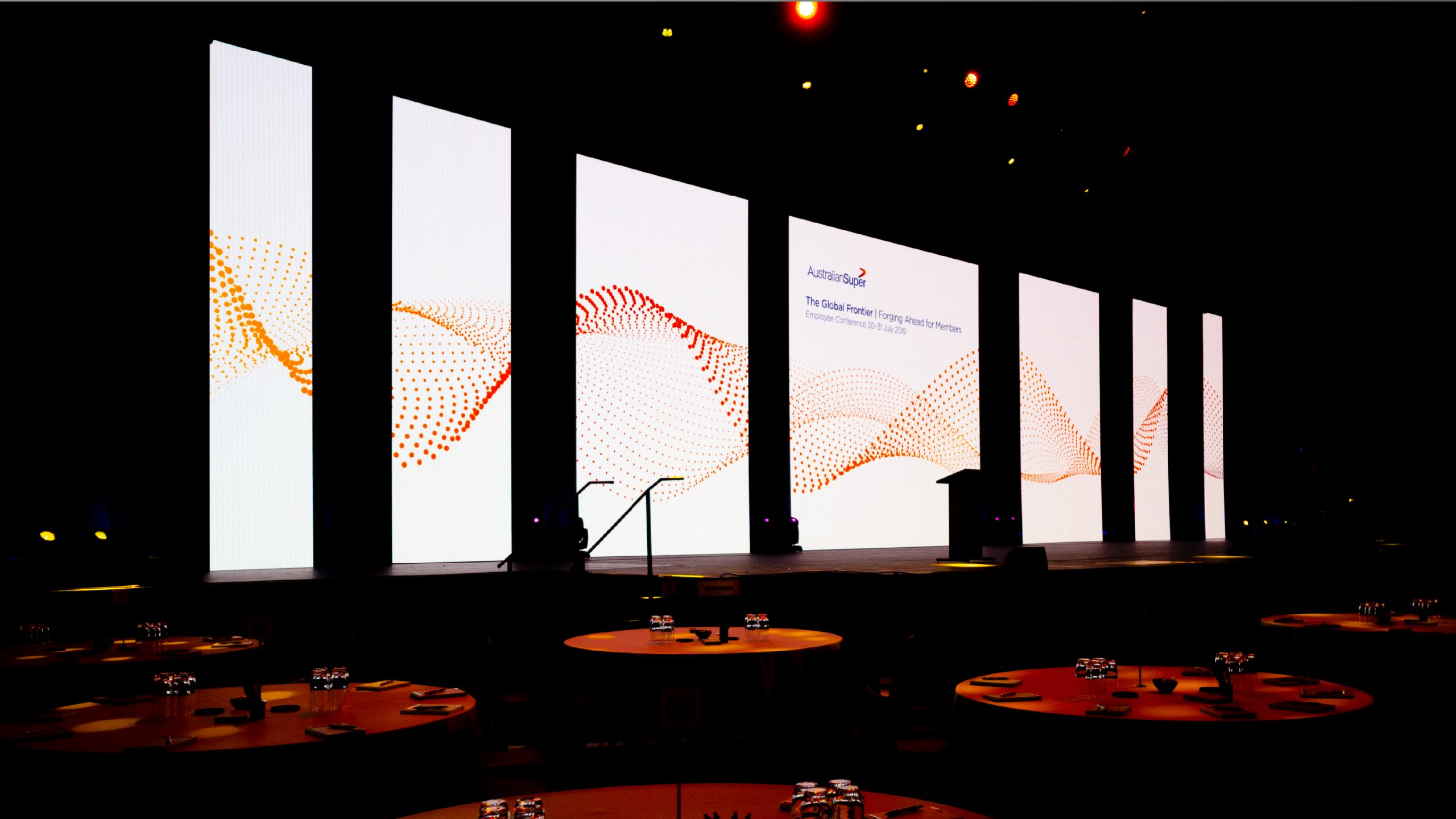 An array of large LED screens on a stage feature the AustralianSuper – Good to Great for Members branding. 