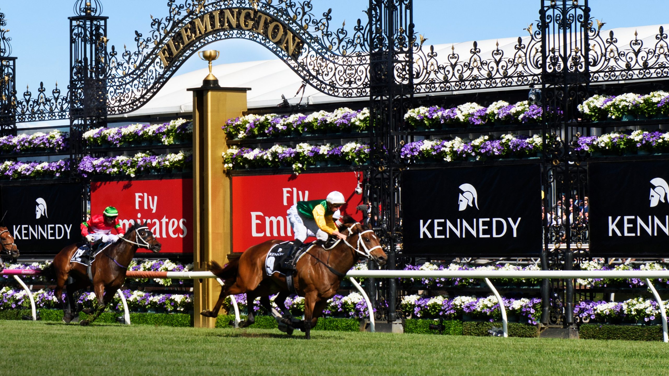 Horses pass the cup in the Kennedy Mile part of the Flemington Race Week. Field branding shows Kennedy logos designed by Helium Design Melbourne.