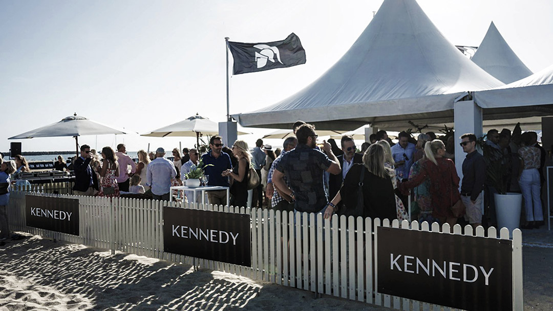 Kennedy beach polo tents featuring black flags with Kennedy branding.
