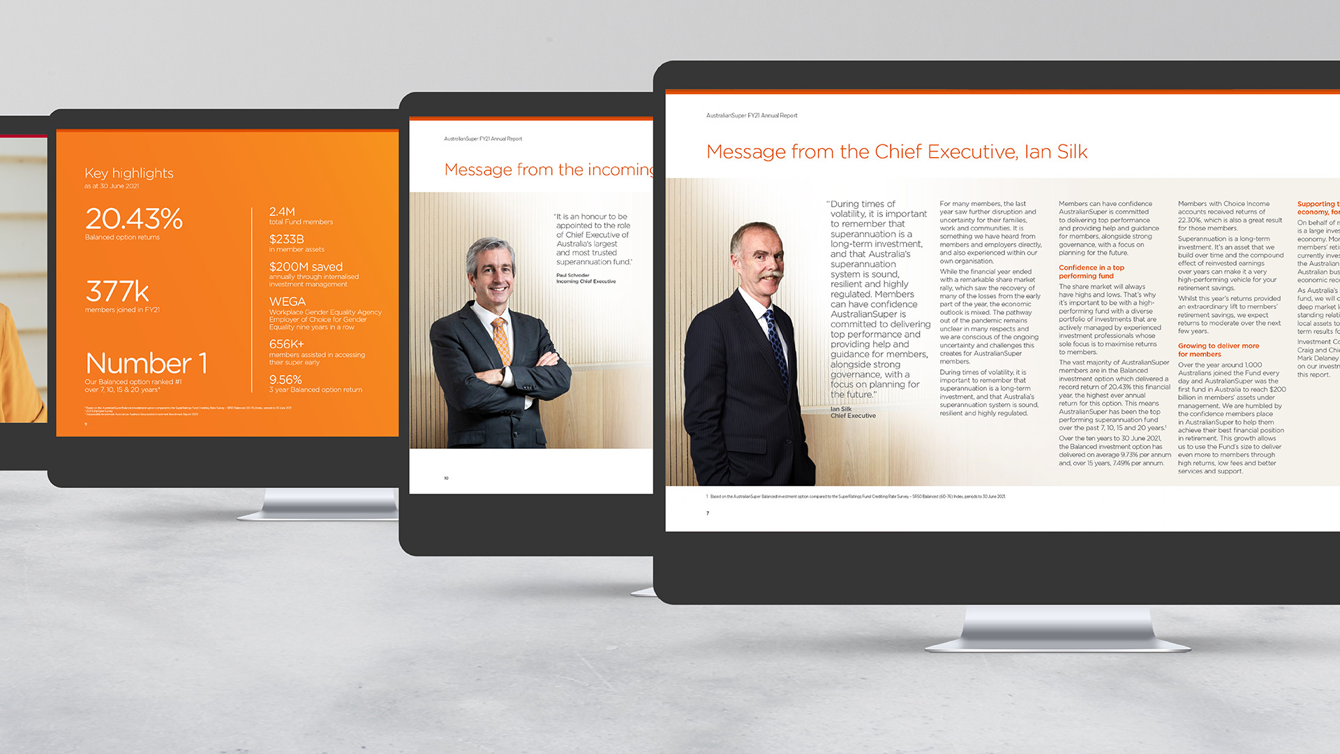Monitors on a desktop displaying the AustralianSuperFY21 Annual Report. Three printed reports stand upright in front of the monitors.